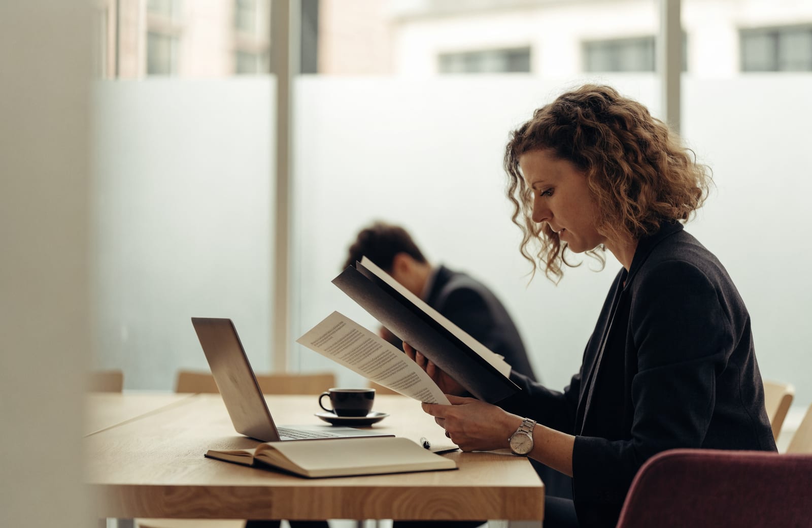 Communicatieprofessional bekijkt een beleidsdossier aan een vergadertafel in een licht kantoor